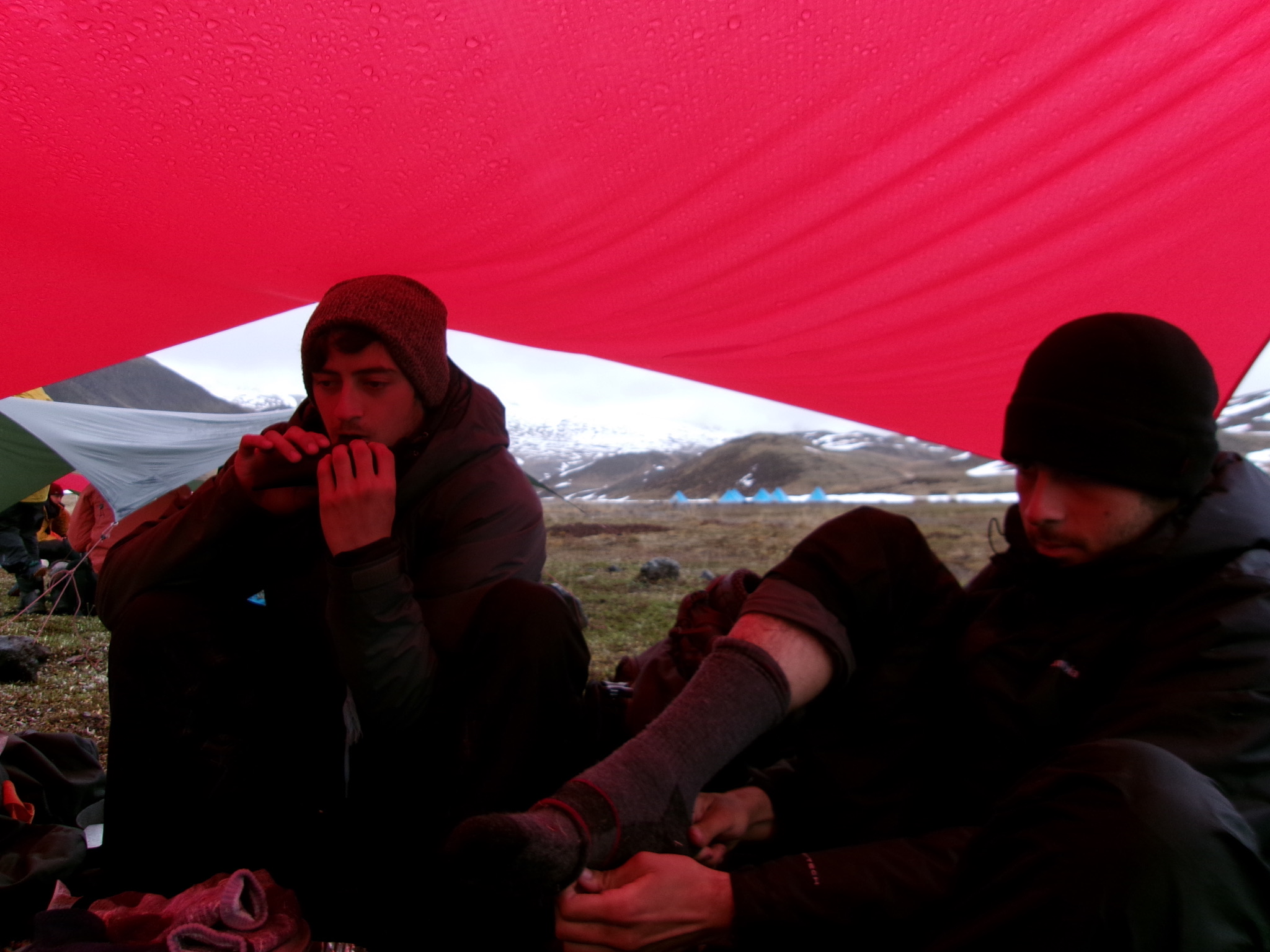Dylan Satow playing harmonica under a red tarp outdoors